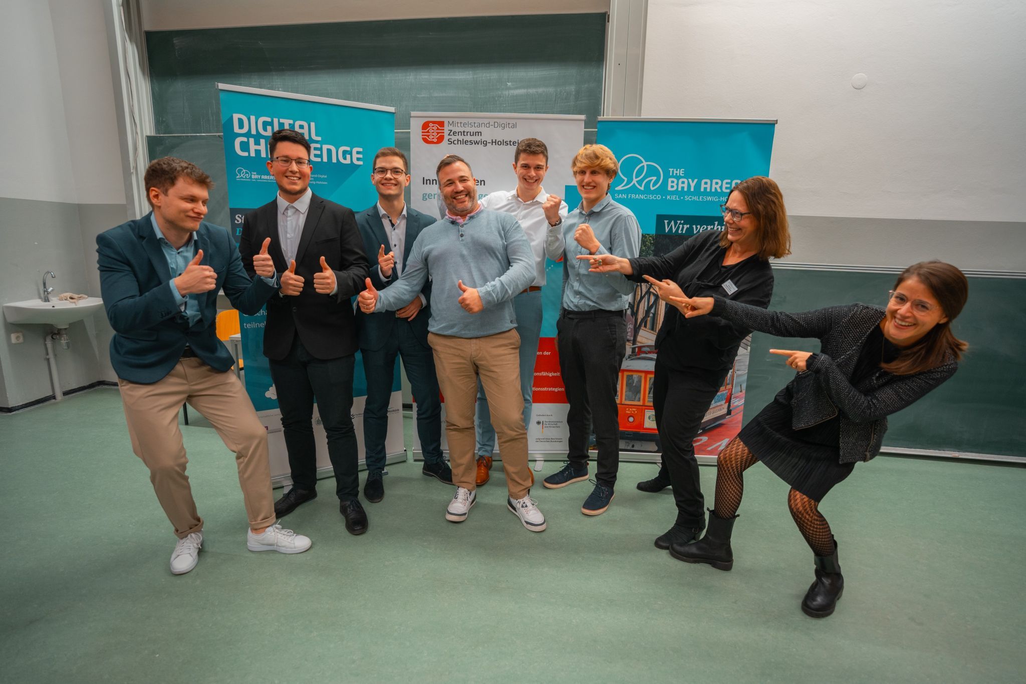 Sieben Männer und Frauen stehen gemeinsam mit IDALABS-Gründer Tobias Gürtler vor mehreren Bannern mit der Aufschrift “Digital Challenge”. Sie lachen und strecken ihre Daumen in die Höhe.
