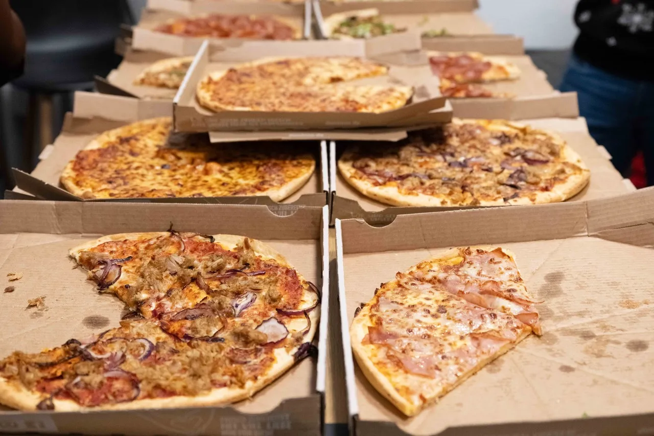 Auf einem Tisch sind neun große Pizzakartons mit unterschiedlich belegten Pizzen ausgebreitet.