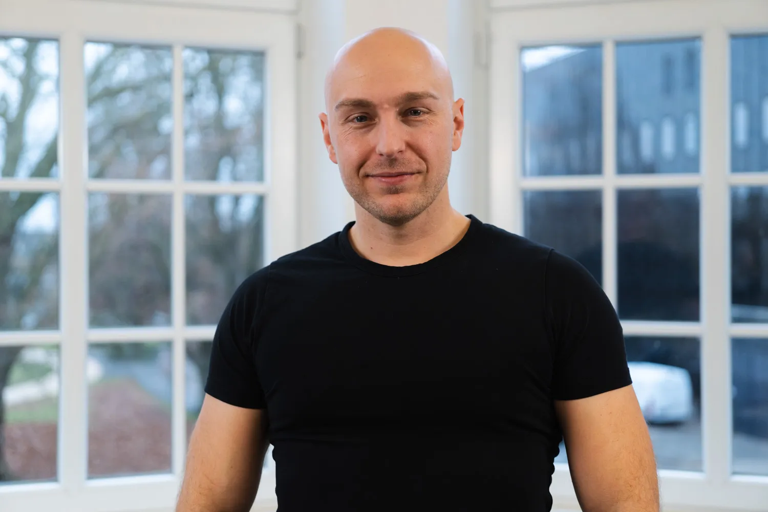 Portrait von IDALABS-Gründer Alexander Westen. Alexander trägt eine Glatze, einen Dreitagebart und ein schwarzes T-Shirt.