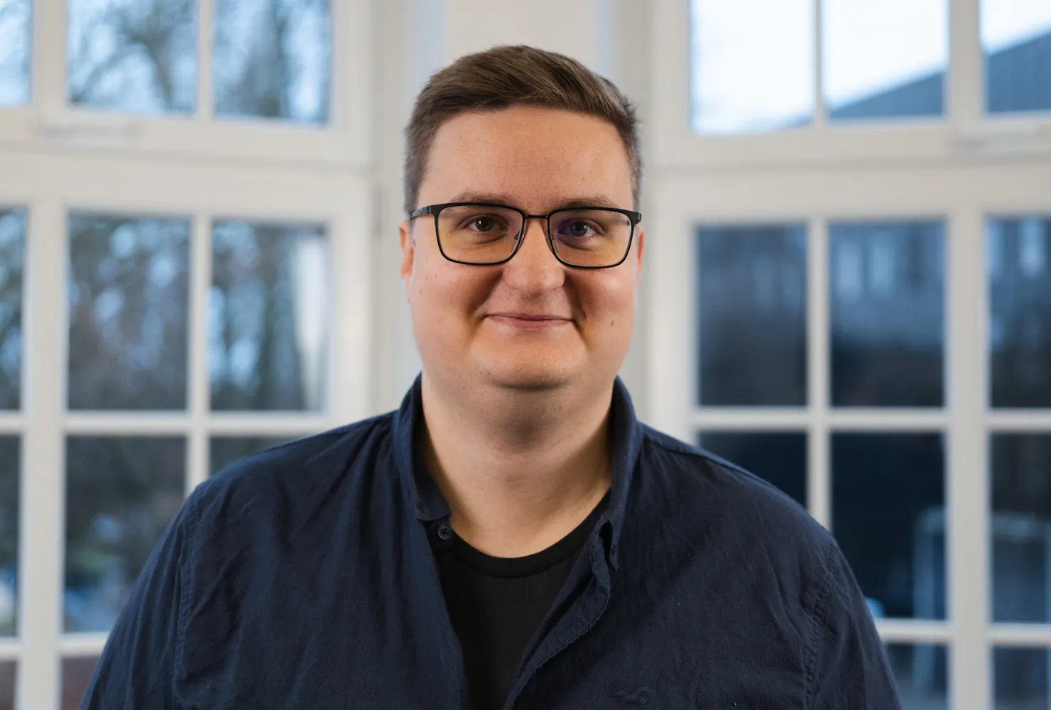 Giovanni A. Paar lächelt in die Kamera. Er trägt eine schwarze Brille, ein dunkelblaues Hemd und kurze, braune Haare.